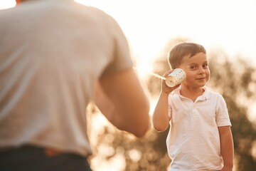 Fun, holding and using string can phone. Father and little son are playing outdoors