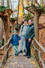 Obraz na płótnie Canvas dad and 2 sons in the autumn forest stand on the bridge. Happy family enjoy the spending vacation together in the nature. father and son hug in the wooden pier at the background river and fall leaves