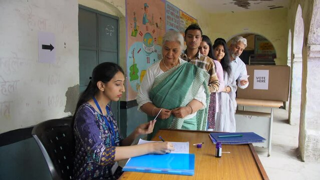 An Indian middle-aged government official verifying the details of the old lady - verification  village elections  identity proof. Candidates standing in queue for the completion of the verificatio...