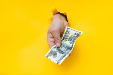 A man's hand holds dirty money through a torn hole in yellow paper. Concept of dishonest income,...