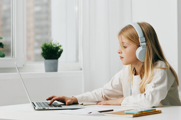 Smiling girl using laptop for elearning at home a cute and happy schoolgirl sitting at a desk,...