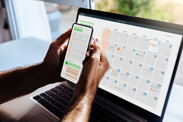Man looking at calendar on phone and laptop, early in the morning for planning the day. Digital schedule concept. - obrazy, fototapety, plakaty