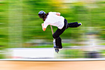 Young man practicing Scootering (Freestyle Scootering) in the new SkatePark in the central park of Igualada, Barcelona, Spain. blurred background