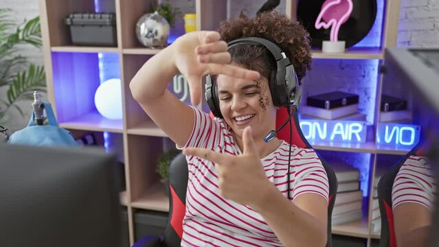Joyful hispanic woman with curly hair, framing her happy face with hands and fingers, making memories in her gaming room. capturing creative photo concepts in the comfort of home.