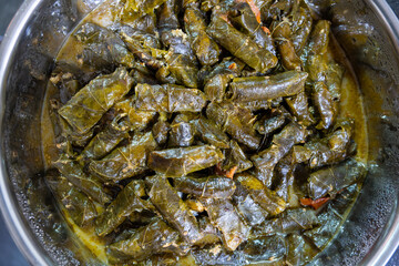 Stainless steel pot full of grape leaves rolls stuffed with rice and ending with it some tomato for flavoring