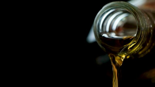 Process of pouring cognac from glass bottle macro slow motion on black background.