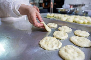 Woman kneads dough with hands in the kitchen on metal tray, pushing it to be flat while using olive oil