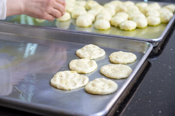 Woman kneads dough with hands in the kitchen on metal tray, pushing it to be flat while using olive oil