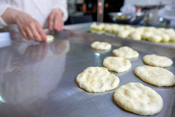 Woman kneads dough with hands in the kitchen on metal tray, pushing it to be flat while using olive oil
