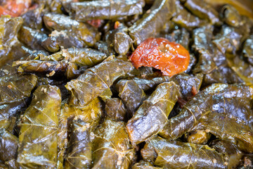 Stainless steel pot full of grape leaves rolls stuffed with rice and ending with it some tomato for flavoring