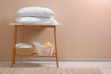 Fototapeta na wymiar Soft pillows and laundry baskets near beige wall indoors. Space for text