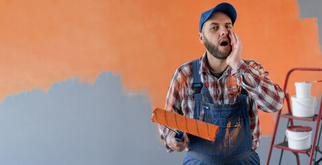 Painter man holding a paint roller standing in room shouting with mouth wide open to the side