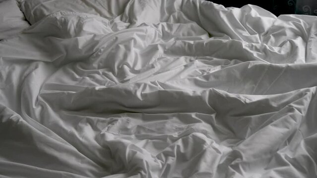 Close-up of unmade bed with white bedsheet and soft blanket in bedroom
