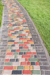 Colorful paved road across lush lawn on sunny day. Pathway with bright step stones in summer park. Creative design element of landscaping