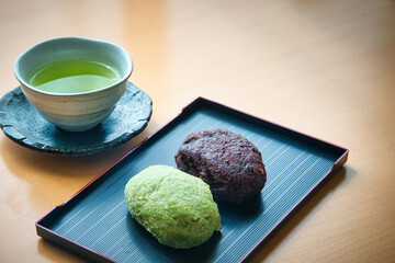 黒い皿に乗った、ずんだあんと粒あんのおはぎと緑茶