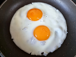 Two fried eggs in a cast iron frying pan for breakfast.