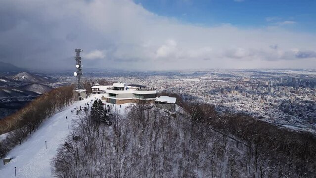 Sapporo, Japan: Aerial drone footage of the observatory at the top of snow covered Mt Moiwa overlooking Sapporo city downtown district in winter in Hokkaido in northern Japan. 