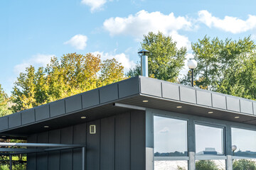 Modern guest house with standing seam facade panoramic glazing and large flat roof overhang in park. Minimalist architectural style of public building