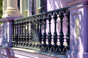 A detailed view of an Italianate porch with intricate railings and balustrade, showcasing the house exterior against a soft lavender background