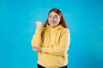 Photo of red haired woman smiling showing thumb empty space recommending isolated blue color...