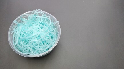 Blue plastic noodles in a plastic container on a gray background, top view