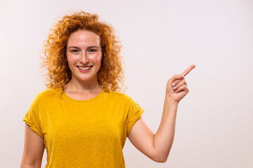 Portrait of beautiful ginger woman pointing on gray background.