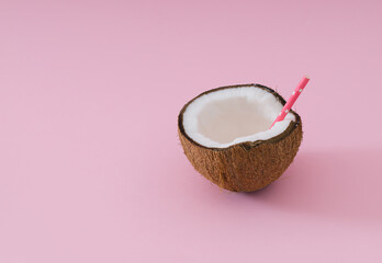Tropical beach concept made of coconut fruit and drinking straw on light pink background. Creative summer idea. Minimal coconut composition.