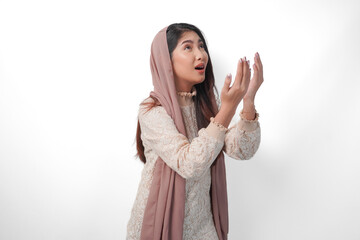 Religious Asian Muslim woman wearing veil headscarf with hands in praying gesture to God, standing over isolated white background. Ramadan and Eid Al Fitr concept