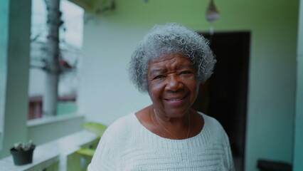 One joyful black elderly 80s woman with gray hair smiling at camera standing at humble domestic...
