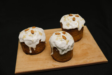 Easter cakes with white icing and almond nuts on a wooden board on a black background. 