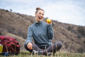Smiling hiker young woman hold yellow apple look at the camera, tourist traveling on weekend getaway,  active lifestyle food camping travel journey adventure discovering tourism hiking concept