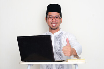 Moslem man sitting in front of laptop smiling and giving thumb up at the camera