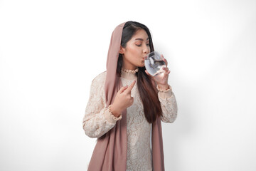 Young Asian Muslim woman wearing headscarf veil feeling thirsty and drinking water after fasting,...