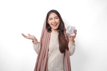 Smiling Asian Muslim woman is holding a glass of water in fasting month over isolated white...