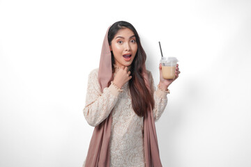 Fototapeta premium Smiling Asian Muslim woman in headscarf veil hijab holding coffee in a plastic cup waiting for iftar to drink. Ramadan concept