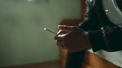 One young black latin man looking at cellphone device screen in bedroom. 20s person of African...