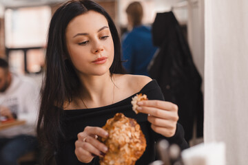 Young brunette woman eating croissants at a cafe. Girl bite piece of croissant look joyful at restaurant. Cheat meal day concept. Teen girl is preparing with appetite to eat croissant.