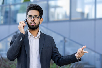 Young, professional businessman in a suit engaging in a conversation on his smartphone outside a modern office building.