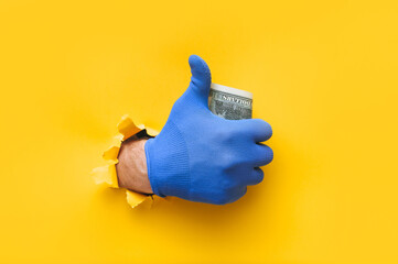 The right male hand in a blue fabric work glove holds dollar bills (money) and shows a thumbs up...