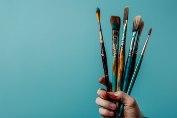 artist holding paintbrushes, isolated on a soft blue background, capturing creativity and artistry - obrazy, fototapety, plakaty