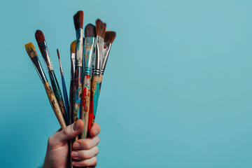artist holding paintbrushes, isolated on a soft blue background, capturing creativity and artistry - obrazy, fototapety, plakaty