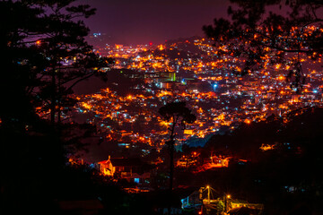 Dazzling night lights of Baguio Cityscape, Philippines, captured from a hill, illuminating the urban area beneath a dark sky.