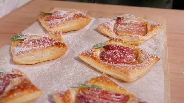 Freshly baked beautiful puff pastries with apples are sprinkled with powdered sugar on a wooden table. Dessert with apples. Homemade fragrant pastries. Close-up, camera moving from bottom to top
