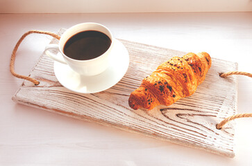 Coffee and croissant on a tray on the windowsill. Traditional breakfast.