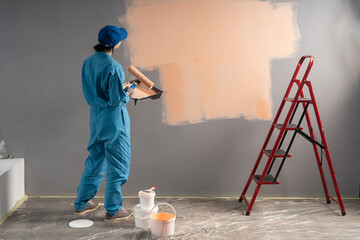 Woman painter standing with paint roller looking at empty wall or space for text, back view