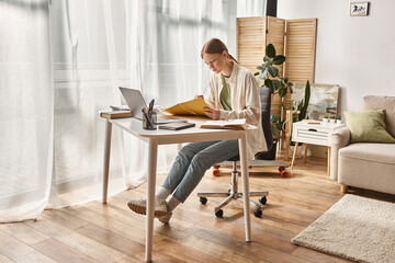 teenage girl taking notes near her laptop while sitting around books, online education concept