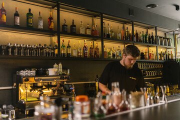 Barman performs process of preparing cocktails standing beside showcase with elite alcohol drinks....