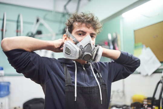 Portrait of a latin young worker adjusting a respiratory protection mask, before starting a painting job in his workshop. Real people at work.