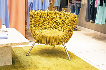 wicker chair with yellow gold threads and fringe in an interior with clothes
