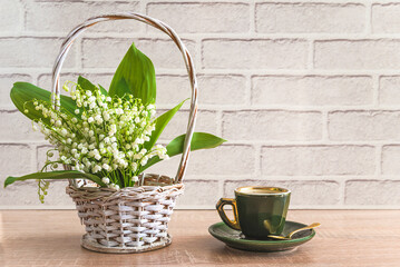 Vintage cup of coffee and bouquet of lilies of the valley in a basket on a wooden table